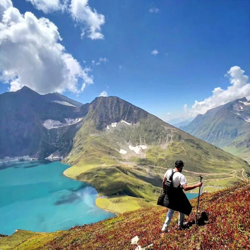 Ali on a ridge high above a glacial lake, back to the camera, walking pole in hand.